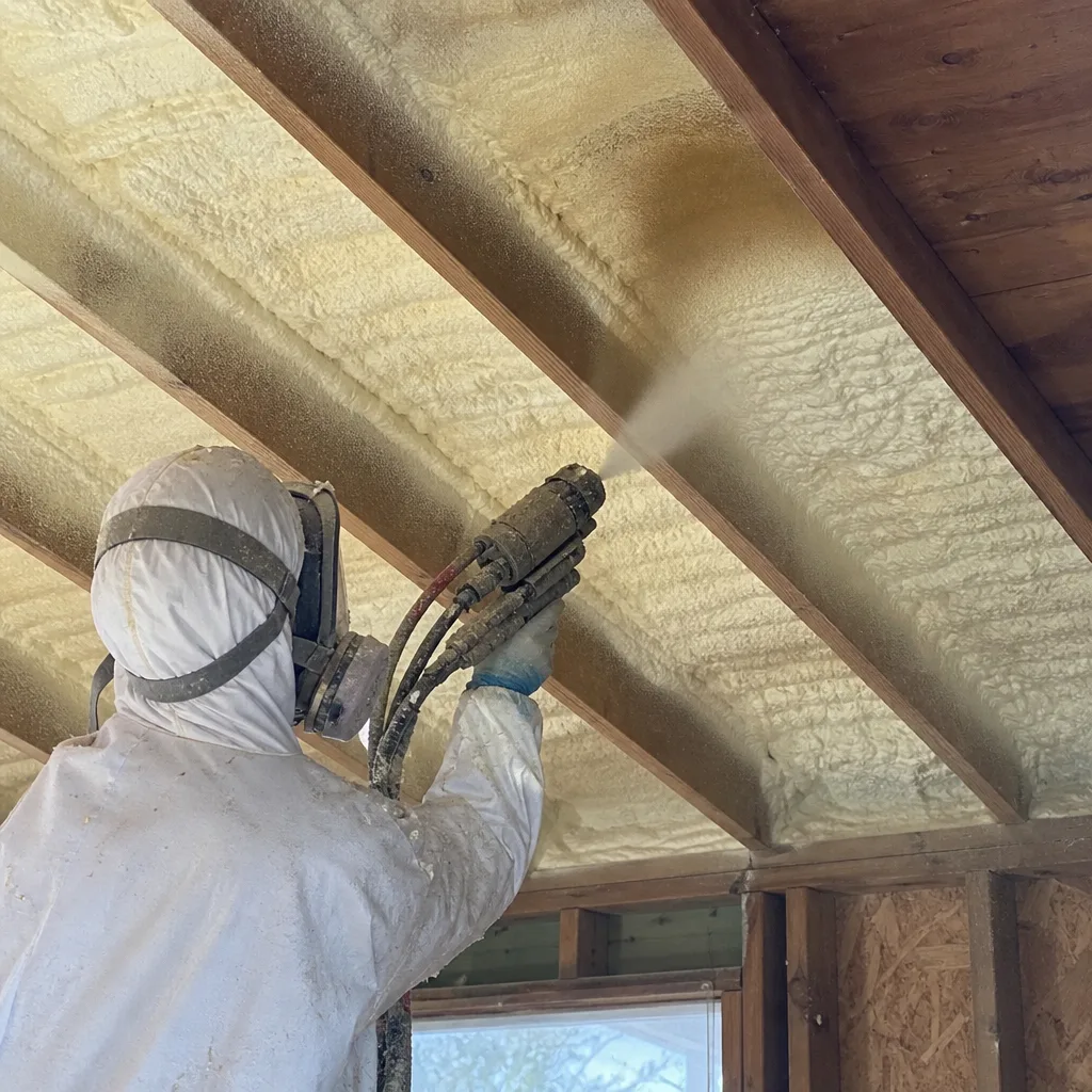 Contractor applying professional spray foam insulation to ceiling joists